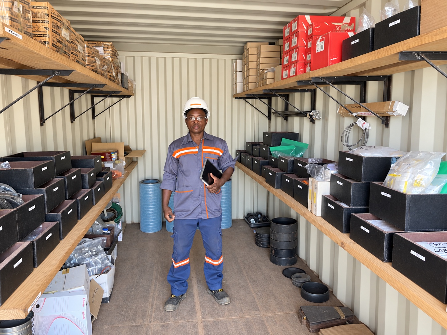Technicien dans le magasin conteneurisé de Kiniéro, entouré des pièces et consommables inventoriés
